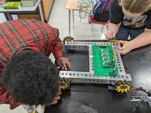 Two female students work on the robot with hand tools